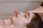 A woman is having a facial at Natasha’s Skin Spa in Southbank Melbourne.  She is lying down with a mask on and a facialist has her hands on her face.