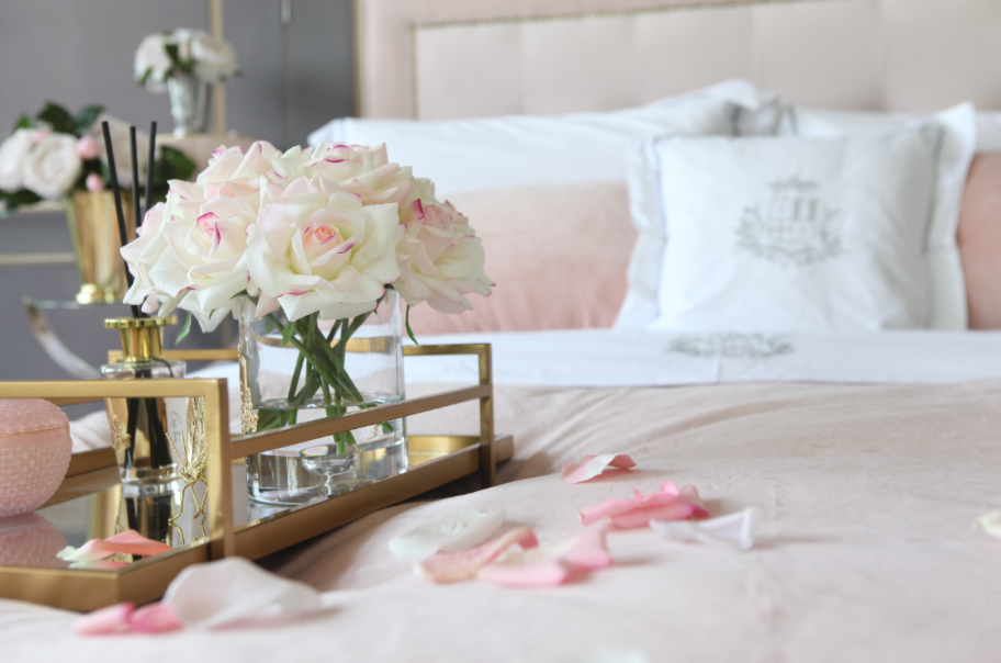 
                  
                    Cote Noire pink roses sitting on a gold tray on the bed in a hotel room with rose petals strewn around
                  
                