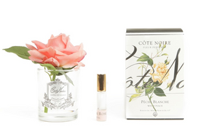 
                  
                    Cote Noire single open rose in white peach shade sits in clear glass vase with a silver crest, beside a bottle of rose petal perfume to scent the rose with, and a gift box, part of our range of flowers for delivery at our facial spa and beauty boutique in Southbank Melbourne Australia
                  
                